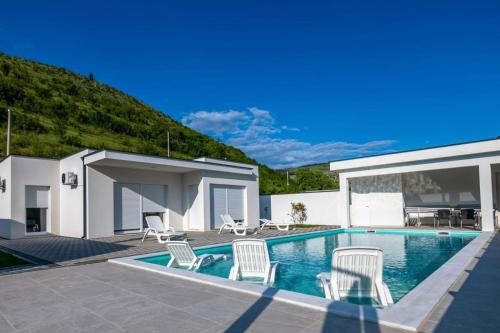 a swimming pool with white chairs and a house at Villas Magnolia in Blagaj