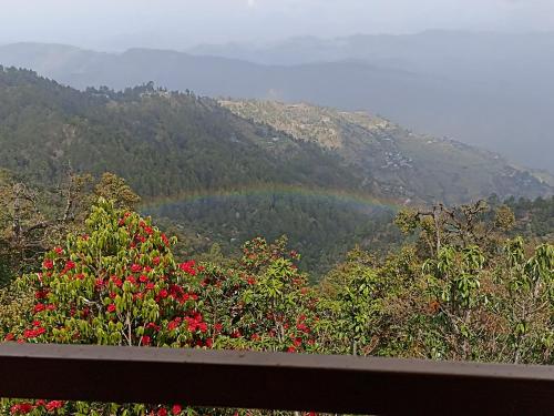 a rainbow over a mountain with trees and red flowers at Nature Valley Homestay Shaukiyathal in Panuānaula
