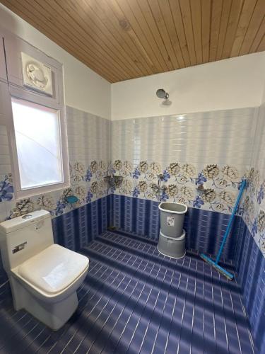 a blue tiled bathroom with a toilet and a window at Kath Kuni Cafe & Stay Shangarh in Shangarh