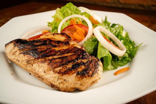 a white plate with a piece of meat and a salad at Minha Glória Hotel Boutique in Bom Jardim