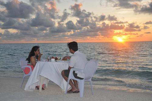 a man and woman sitting at a table on the beach at Rasdhoo Coralville in Rasdu