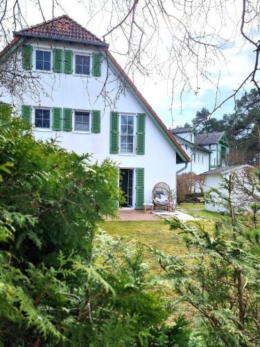 a white house with green shutters at Düne 4 - Ferienunterkunft mit eigenem Garten in der beliebten Dünenresidenz - sanftes Meeresrauschen inklusive in Ostseebad Karlshagen