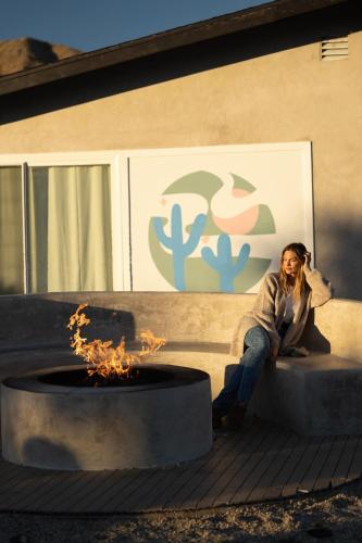 a woman sitting on a bench next to a fire pit at Hotel California By The Cohost Company in Morongo Valley