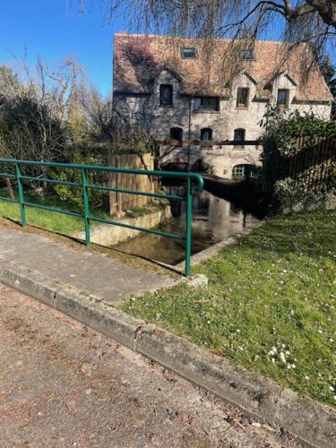 a green fence next to a river with a building at Le Moulin de Dannemarie in Dannemarie
