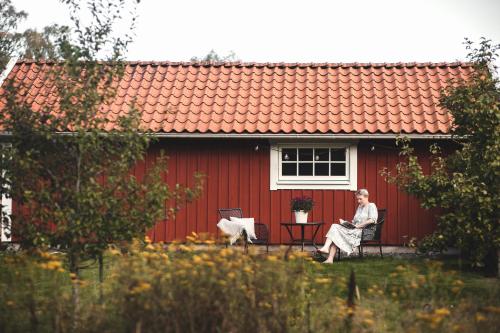 a man sitting in a chair in front of a red house at Smålandstorpets lanthotell in Hok