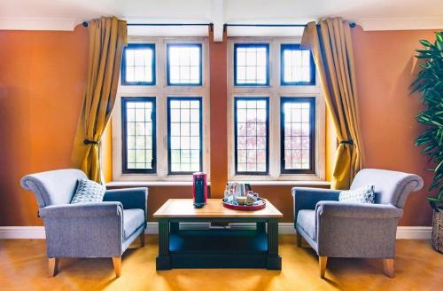 a living room with two chairs and a table and windows at Cricklade House Hotel, Sure Hotel Collection by Best Western in Cricklade