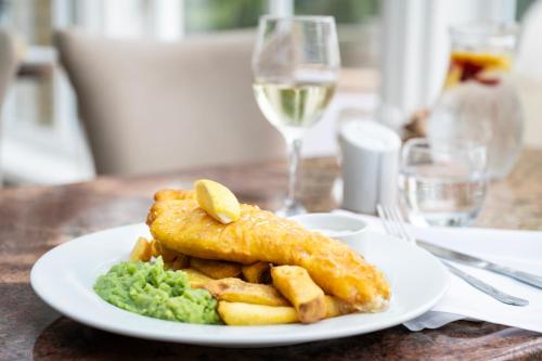 a plate of food with fish and chips and a glass of wine at Cricklade House Hotel, Sure Hotel Collection by Best Western in Cricklade