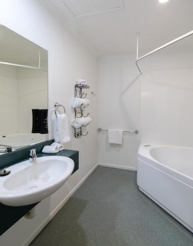 a white bathroom with a sink and a tub at Camelot Motor Lodge and Conference Centre in Palmerston North