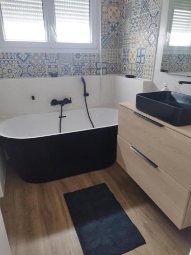 La salle de bains est pourvue d'une baignoire noire et d'un lavabo. dans l'établissement Cozy House, à Angers