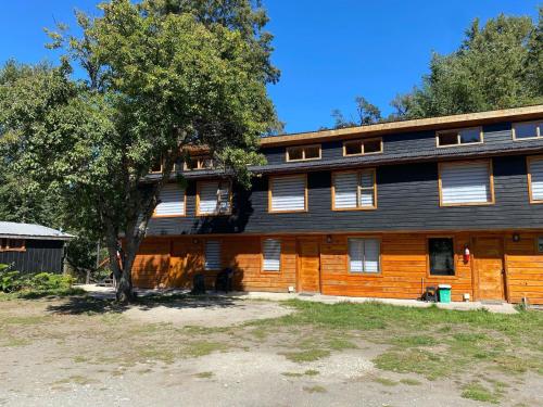 a large wooden house with a tree in front of it at Cabañas Camping Río Fuy in Neltume