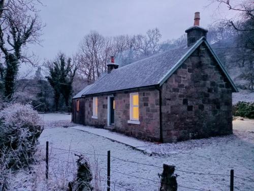 a small stone house in the snow with a fence at Red Deer Cottage at Fanans in Oban