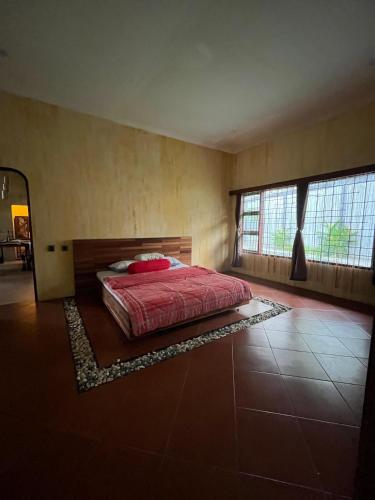 a bedroom with a bed with a red comforter and two windows at D'Kastil Jogja in Cepit