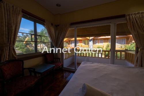 a bedroom with a bed and a balcony with windows at 4 Bedroom Log Cabin in Camp John Hay Baguio in Baguio