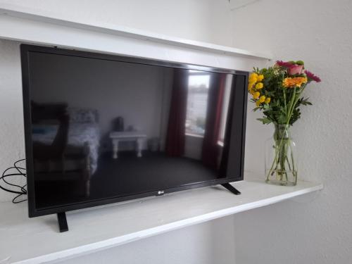 a flat screen tv sitting on a shelf with a vase of flowers at Freedom Park Villas, Plymouth in Plymouth