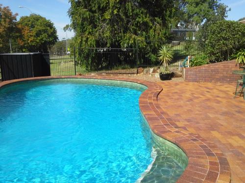 a swimming pool with a brick walkway around it at Hideaway Motor Inn in Armidale