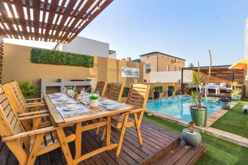 un tavolo e sedie in legno su un patio con piscina di The Sandcastle Guesthouse - Melkbosstrand a Melkbosstrand