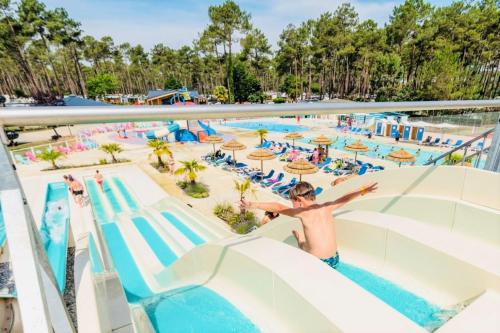 - une piscine dans un complexe avec un garçon descendant un toboggan dans l'établissement MH 353 LUMINOSA 3chambres et 2 salles de bains dans camping 4 étoiles, à Saint-Julien-en-Born