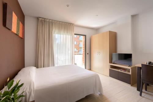 a bedroom with a white bed and a television at SG Costa BCN Apartments in Castelldefels