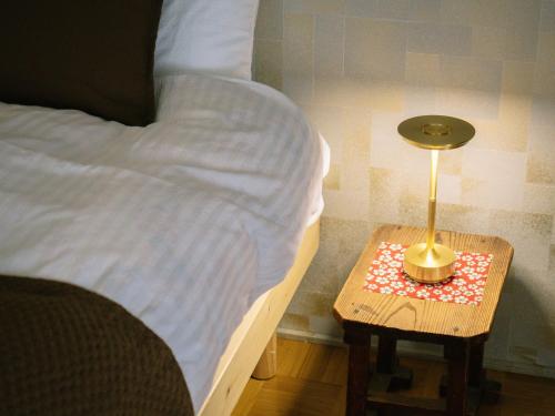 a bed with a side table with a lamp on it at お宿のごえん in Shijonawate
