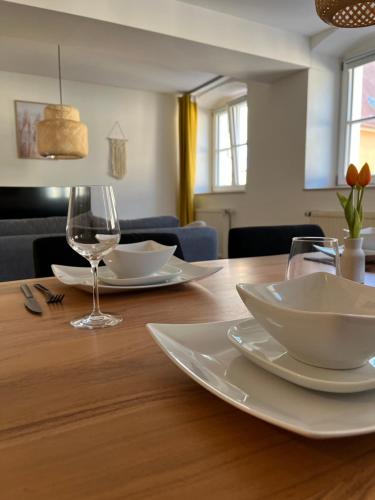a wooden table with white plates and a wine glass at traumhafte Business & Relax Wohnung direkt im Stadtkern Oettingens by Elation Homes in Oettingen in Bayern