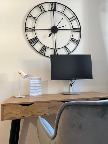 a desk with a monitor and a clock on the wall at traumhafte Business & Relax Wohnung direkt im Stadtkern Oettingens by Elation Homes in Oettingen in Bayern