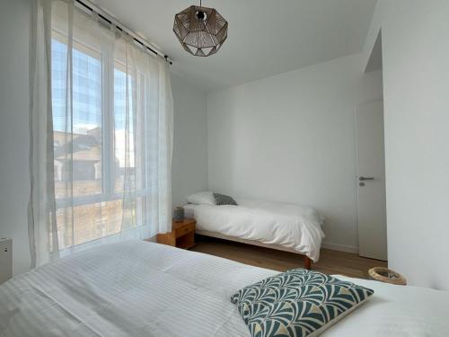 a white bedroom with two beds and a window at Soleil couchant in Roscoff