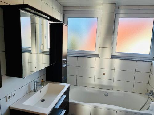 a bathroom with a sink and a tub and two windows at Burgblick Wohnung in Stetten bei Hechingen