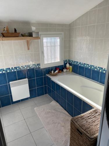- une salle de bains bleue et blanche avec baignoire et fenêtre dans l'établissement Maison à la mer, à Sainte-Marie-la-Mer