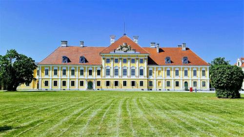 a large yellow building with a red roof on a grass field at Vila Velebita in Vukovar