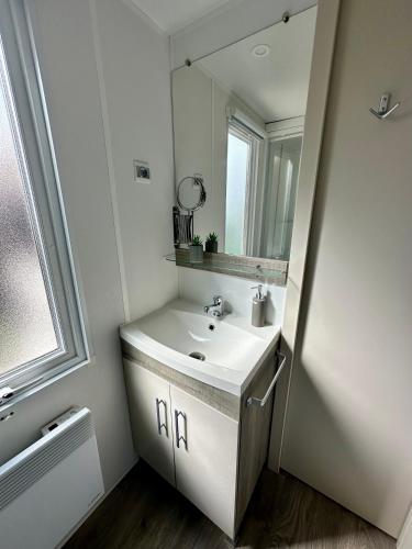 une salle de bain blanche avec un lavabo et un miroir dans l'établissement Mobil home Happiness33 dans camping 5 étoiles accès direct plage Vendays Montalivet, à Vendays-Montalivet