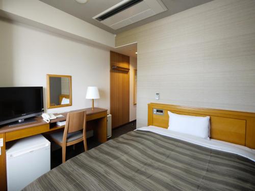 秋田市にあるホテルルートイン秋田土崎のベッド、デスク、テレビが備わるホテルルームです。