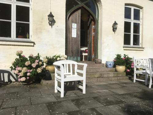 two white chairs sitting outside of a house with flowers at Hostel California in Hinge