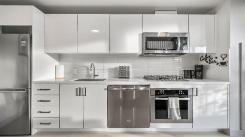 a kitchen with white cabinets and stainless steel appliances at Miso 2 BD - Skyline View Patio Gym Pool & AC in Calgary