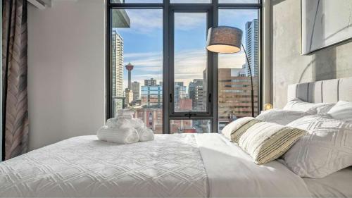 a bedroom with a white bed with a large window at Miso 2 BD - Skyline View Patio Gym Pool & AC in Calgary