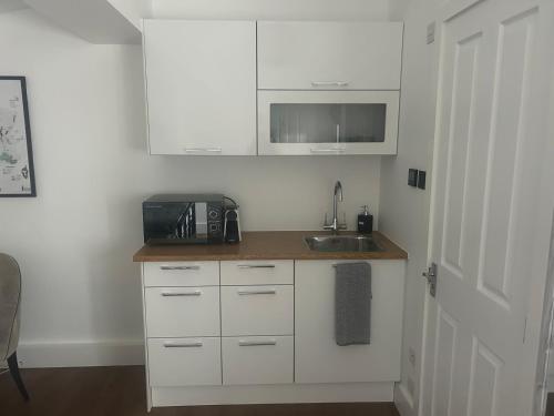 a kitchen with white cabinets and a sink and a microwave at Spacious studio with free EV recharge overnight in Watford
