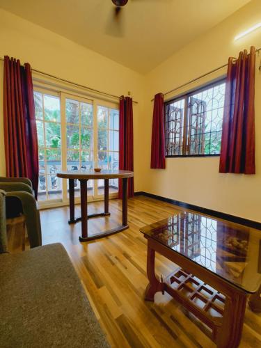 a living room with a table and some windows at Susegad Shores - Chic 1BHK Coastal Escape in Siolim