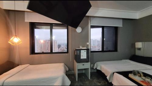 a room with two beds and a tv and windows at Golden Flat's - Slaviero Guarulhos in Guarulhos