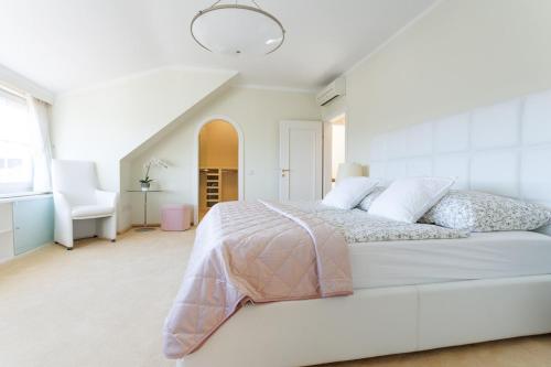 a white bedroom with a large bed and a chair at Luxury Villa with Indoor Pool, Jacuzzi, Sauna & Breathtaking City View in Klosterneuburg