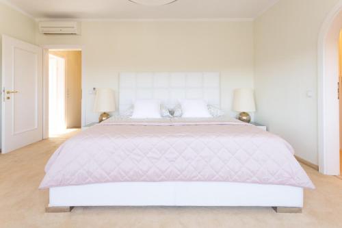 a white bedroom with a large bed with two lamps at Luxury Villa with Indoor Pool, Jacuzzi, Sauna & Breathtaking City View in Klosterneuburg