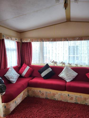 a red couch with pillows sitting in front of a window at Kerrys Place, 75 Sealands Caravan Site, Ingoldmells 6 Berth in Ingoldmells