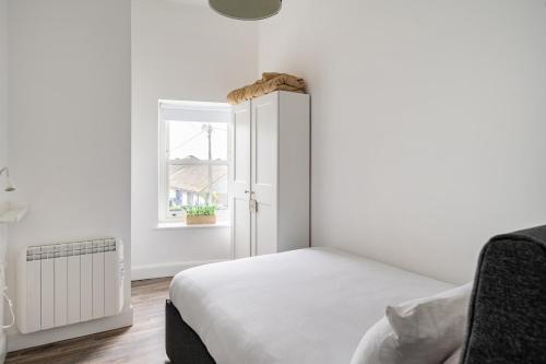 a white bedroom with a bed and a window at 1 Cathedral Place - Cathedral Townhouses Cobh in Cobh