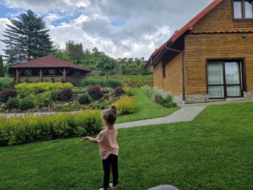a little girl standing in the grass near a house at Bieszczady Domek u Pączka in Polańczyk
