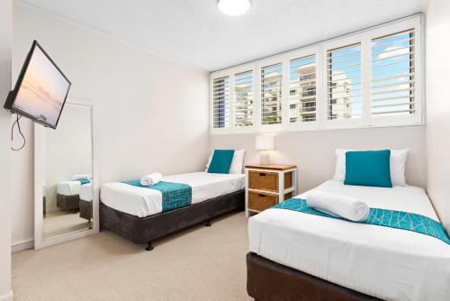 a bedroom with two beds and a mirror at Northwind Beachfront Apartments in Mooloolaba