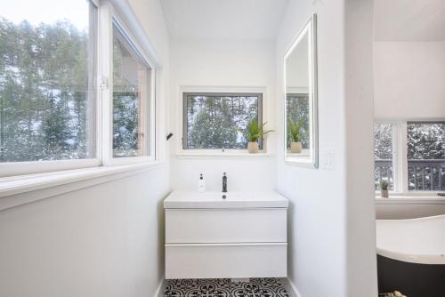 a white bathroom with a sink and two windows at Boulder Luxury Getaway 7 acres River & Pond in Boulder