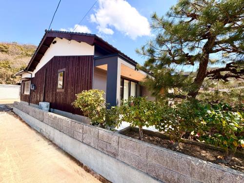 a small house on a retaining wall next to a tree at My Place 小豆島 1日1組限定 海近の贅沢ステイ 2025年フルリノベ 洗練モダンデザイン 最大8名 一棟貸切 in Tonosho