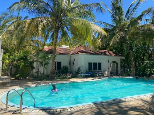 a man in a swimming pool in front of a house at Maasai Koroga Hotel & Apartments in Mombasa