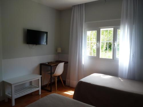 a bedroom with a bed and a desk and a window at Hostal Las Cumbres in Conil de la Frontera