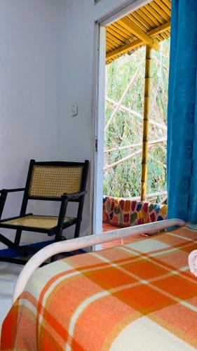 a bed and a chair in a room with a window at Hostal El Mirador in Minca
