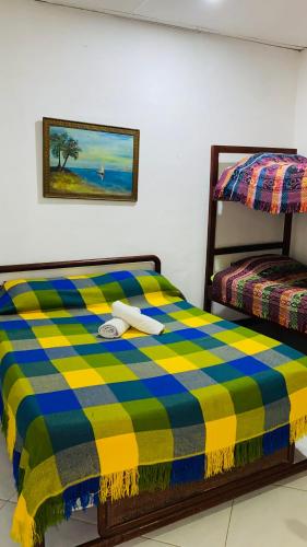 a bed with a yellow and blue checkered blanket at Hostal El Mirador in Minca