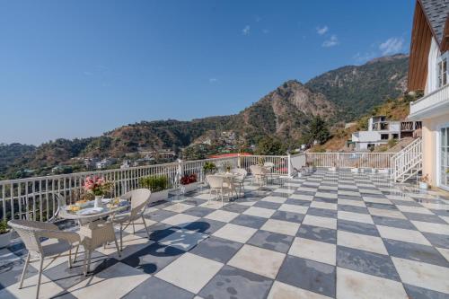 a balcony with chairs and tables and mountains at SaffronStays The Rajpur in Rājpur